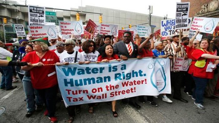 A faixa em primeiro plano diz: "Água é um direito humano. Forneça água! Taxe Wall Street!"
